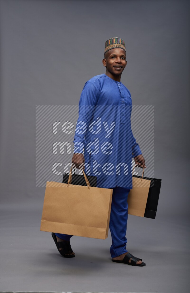Man wearing Nigerian outfit standing holding shopping bag on gray background