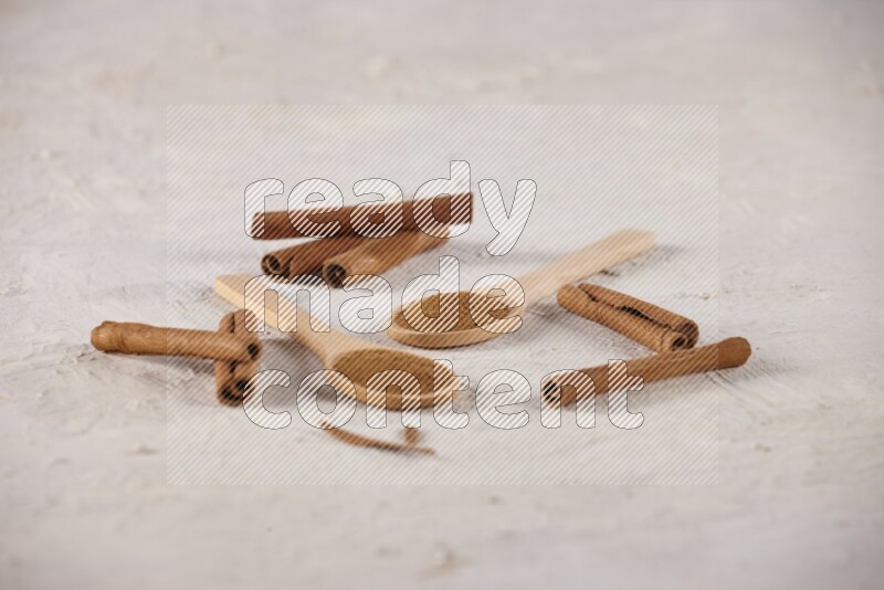 Two wooden spoons full of cinnamon powder with cinnamon sticks on white background