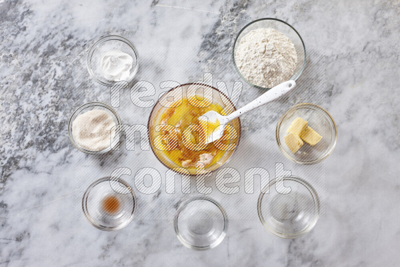 كوكيز خطوة بخطوة بمكوناتها، الدقيق، الزبدة، السكر البني، البيض، الفانيليا، السكر الأبيض، رقائق الشوكولاتة وصودا الخبز على خلفية رخام رمادي