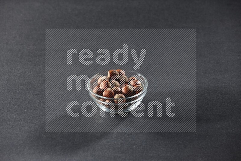 A glass bowl full of hazelnuts on a black background in different angles