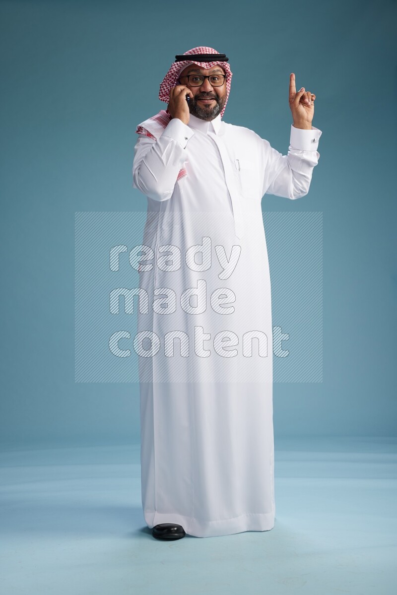 Saudi Man with shimag Standing talking on phone on blue background