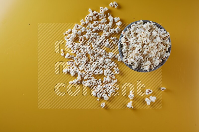 A multicolored pottery bowl full of popcorn with popcorn beside it on a yellow background in different angles