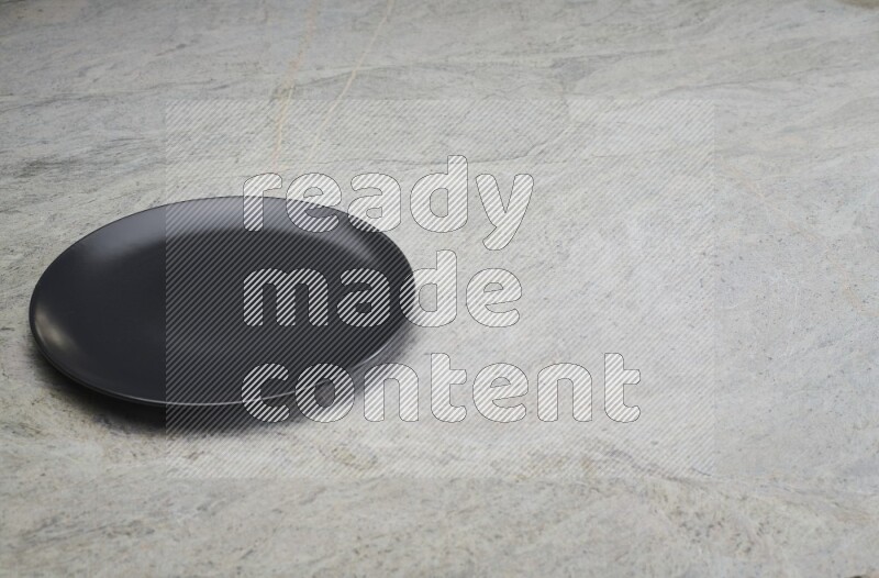 A black ceramic circular plate on grey marble background