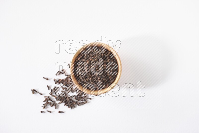 وعاء خشبي ممتلئ بالقرنفل مع حبوب متناثرة على أرضية بيضاء