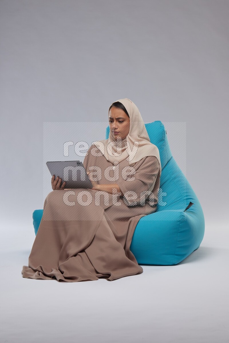 A Saudi woman sitting on a blue beanbag and working on tablet