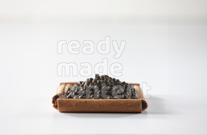 أربعة من أعواد القرفة مكونة شكل مربع بداخلها حبوب الفلفل الأسود علي خلفية بيضاء