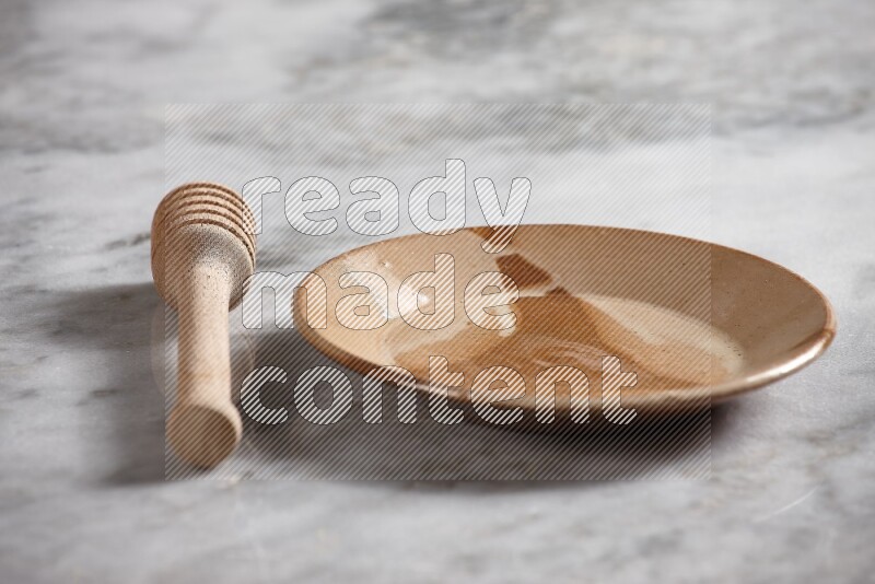 Multicolored pottery plate with wooden honey dipper on the side on grey marble background