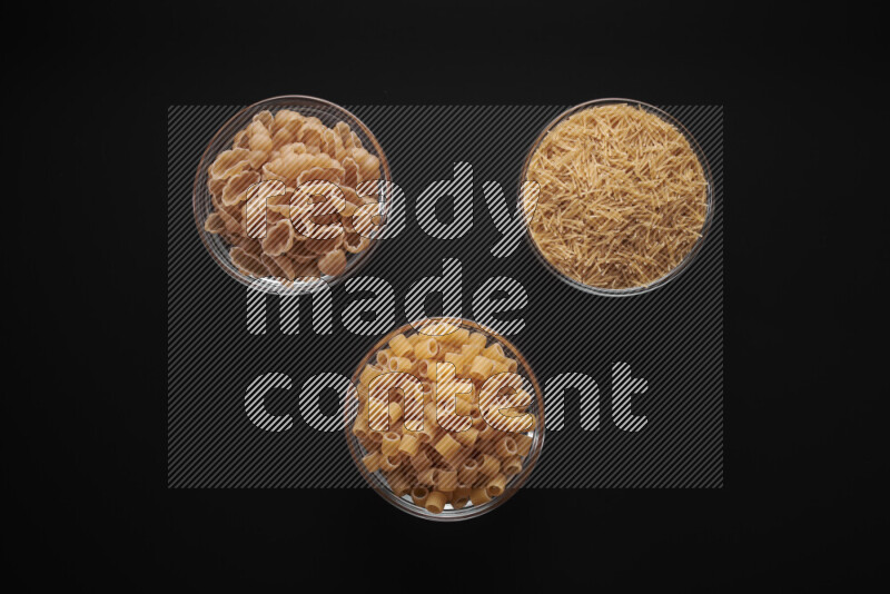 Different pasta types in glass bowls on black background
