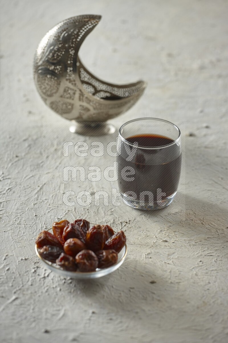 A silver lantern with different drinks, dates, nuts, prayer beads and quran on textured white background