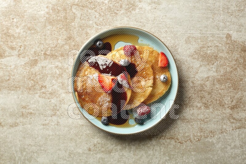 Three stacked mixed berries pancakes in a blue plate on beige background
