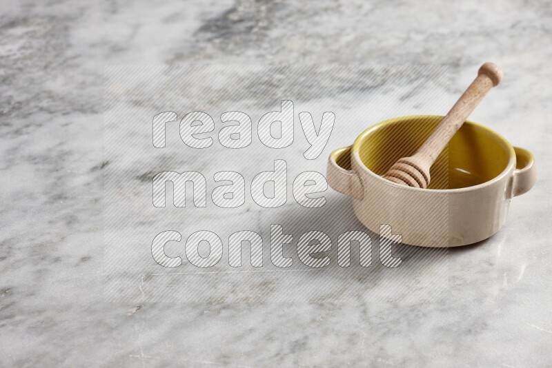 Multicolored pottery bowl with wooden honey dipper in it on grey marble background