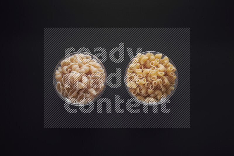 Different pasta types in glass bowls on black background