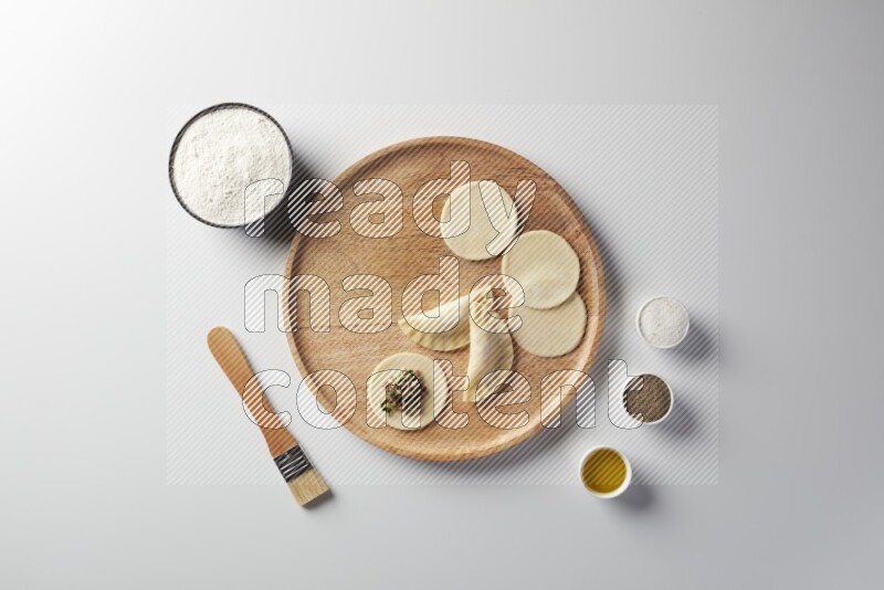 two closed sambosas and one open sambosa filled with meat while flour, salt, black pepper and oil with oil brush aside in a wooden dish on a white background