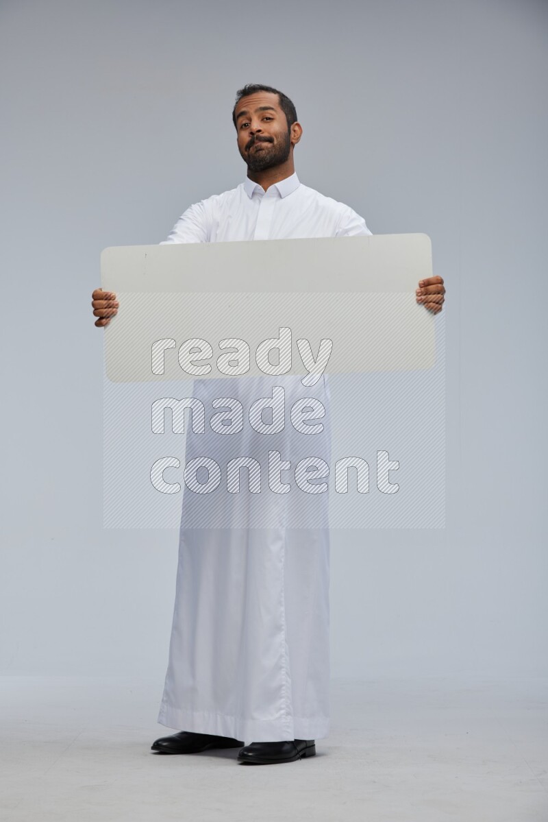 Saudi man wearing Thob standing holding board on Gray background