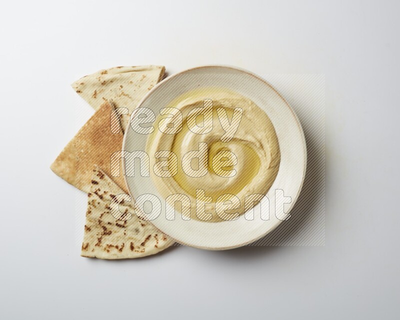 Hummus in a pottry plate garnished with olive oil on a white background
