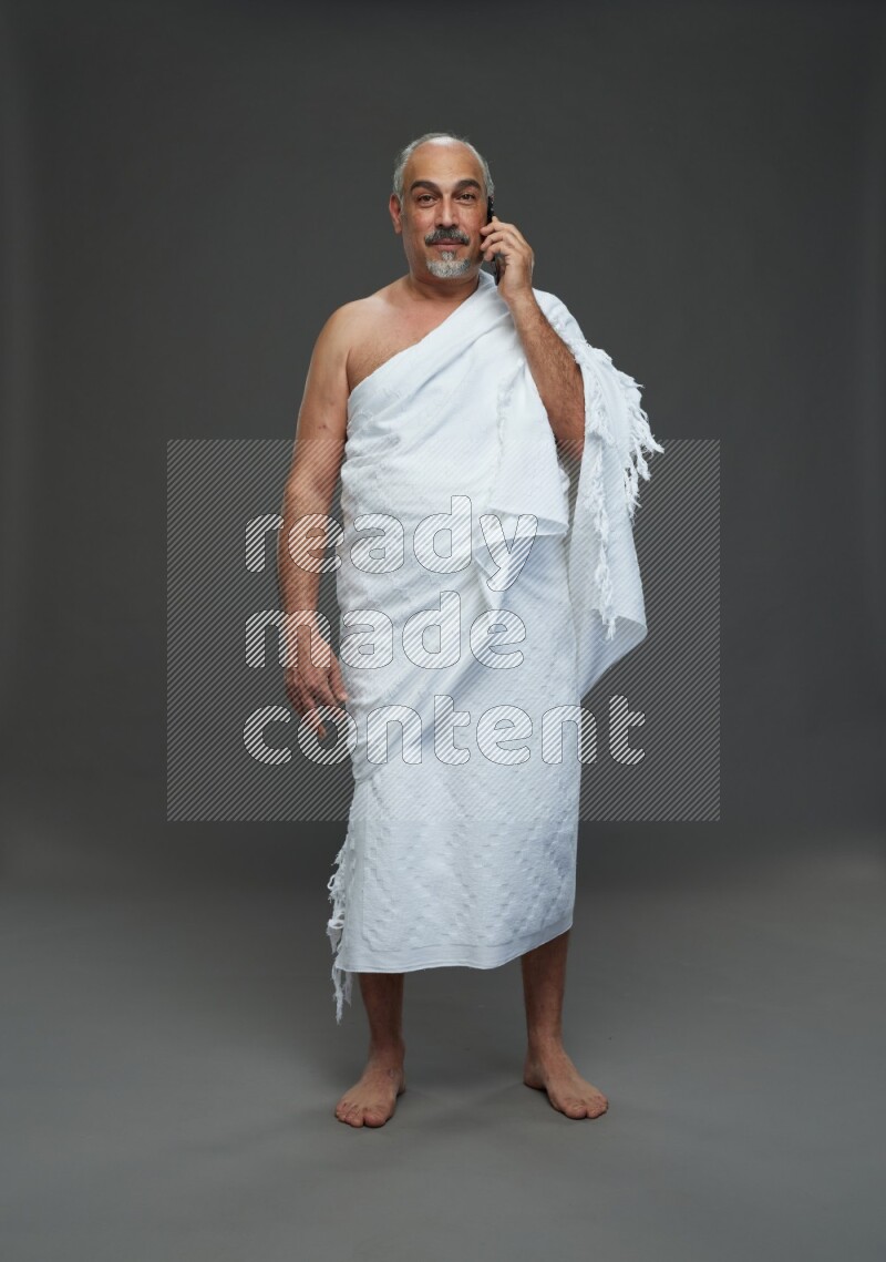 A man wearing Ehram Standing talking on phone on gray background