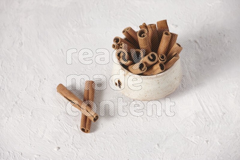 Cinnamon sticks in a beige bowl on a white background