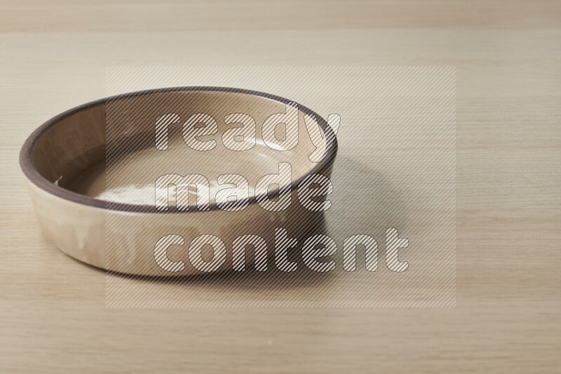 وعاء فرن فخاري باللون البيج على خلفية خشبية فاتحة