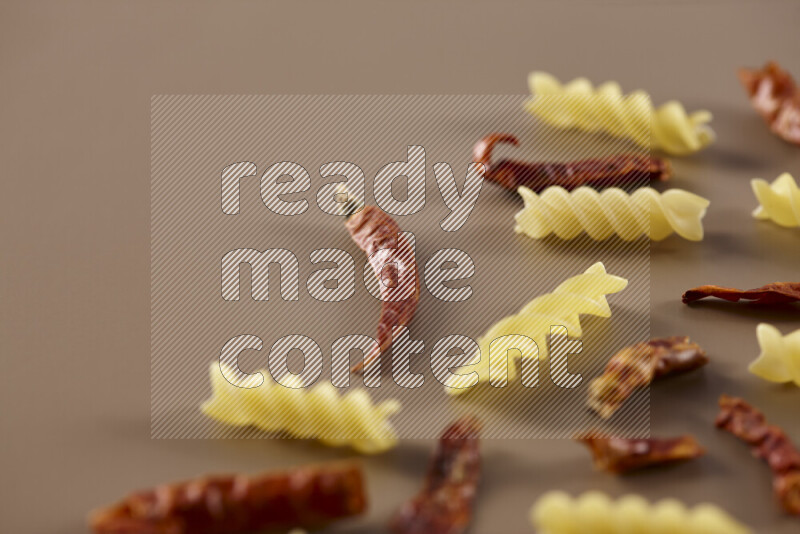 Raw pasta with different ingredients such as cherry tomatoes, garlic, onions, red chilis, black pepper, white pepper, bay laurel leaves, rosemary and cardamom on beige background