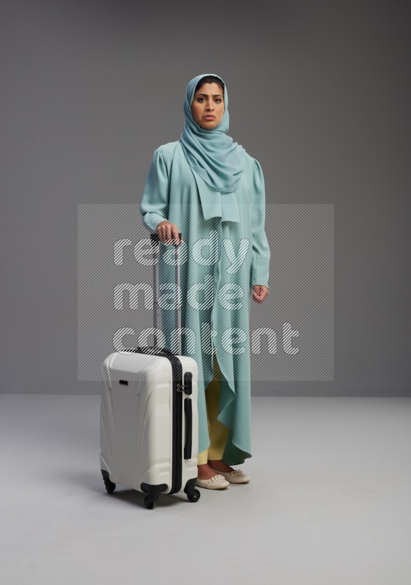 Saudi Woman wearing Abaya standing holding Travel bag on Gray background
