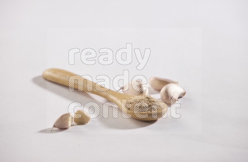 A wooden spoon full of garlic powder with cloves beside it on a white flooring