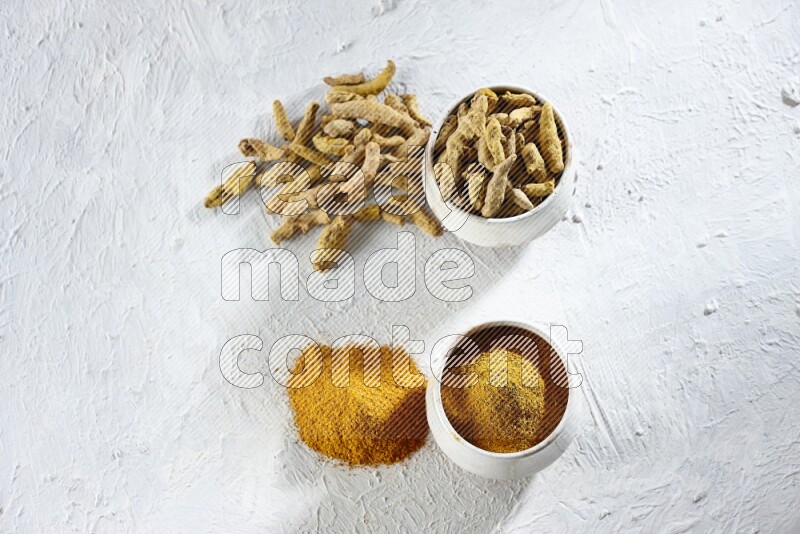 2 beige pottery bowls full of turmeric powder and dried turmeric whole fingers with powder and fingers next of it textured white flooring