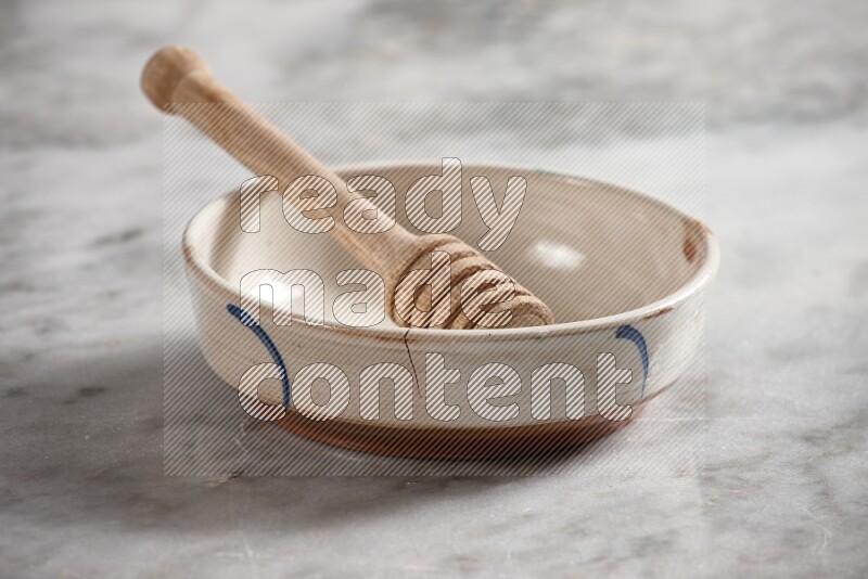 Multicolored pottery bowl with wooden honey dipper in it on grey marble background