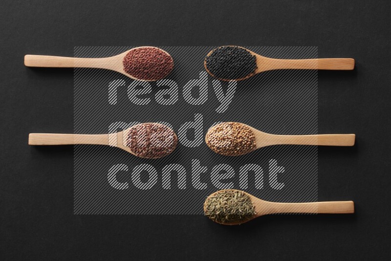 wooden spoons filled with white peppers, mustard seeds, black seeds, garden cress, cumin and flax on black flooring