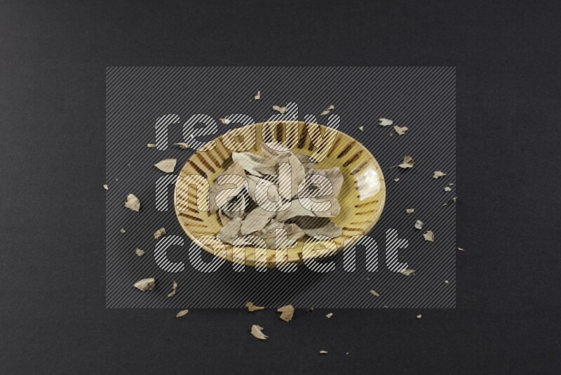 صحن فخاري متعدد الألوان ممتلئ بأوراق الغار المجففة على أرضية سوداء