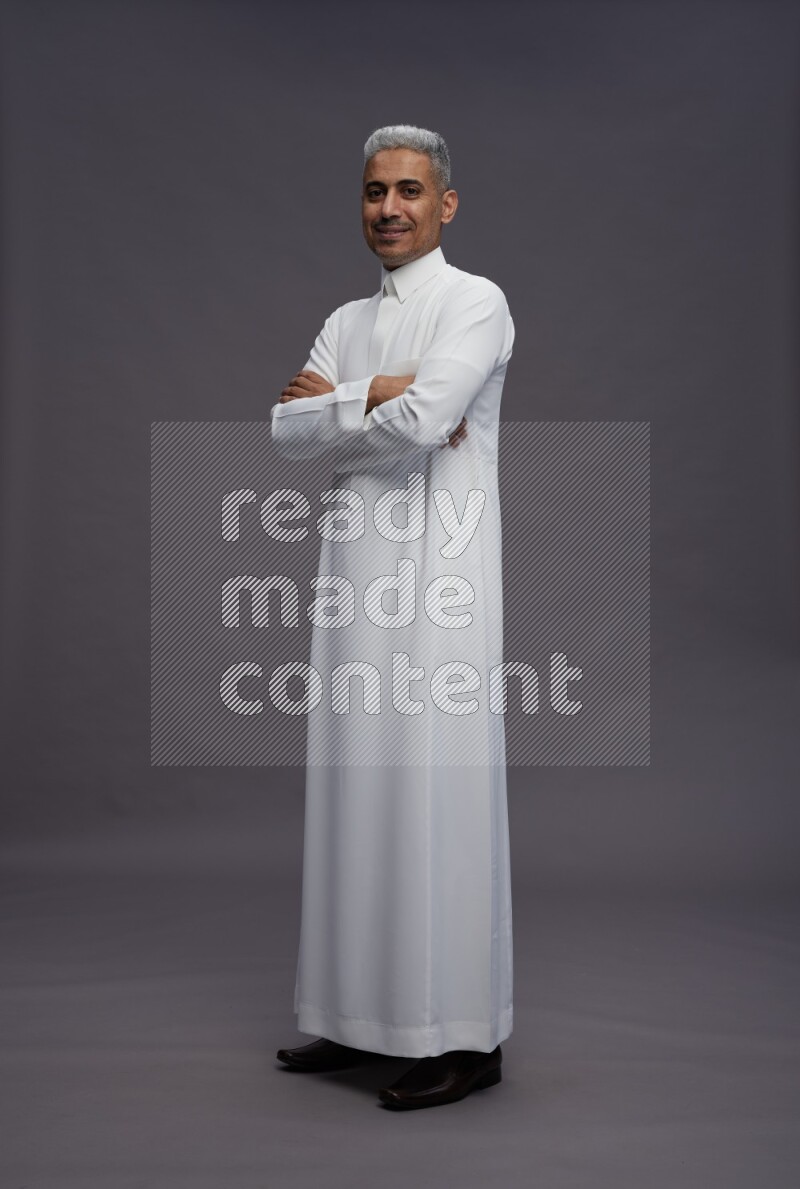 Saudi man wearing thob standing with crossed arms on gray background