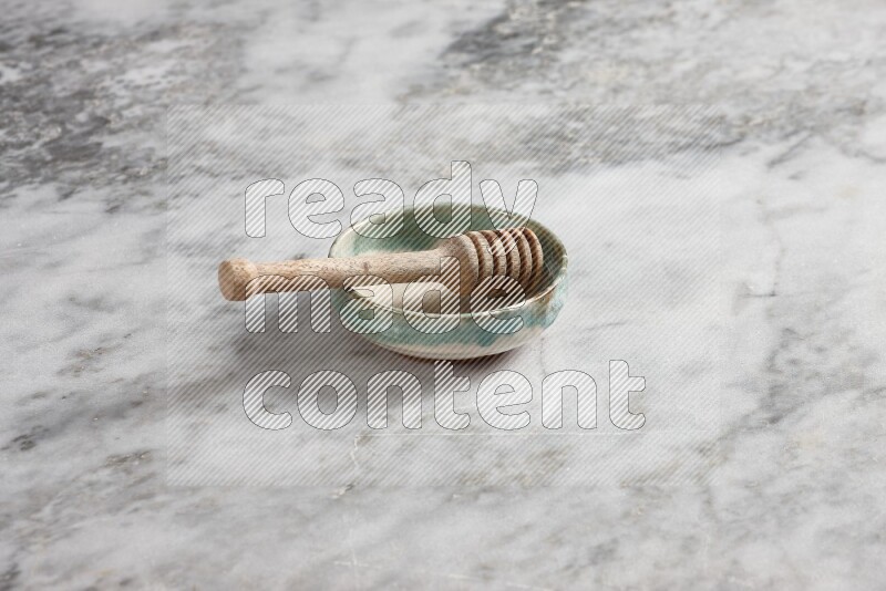 Multicolored pottery bowl with wooden honey dipper in it on grey marble background
