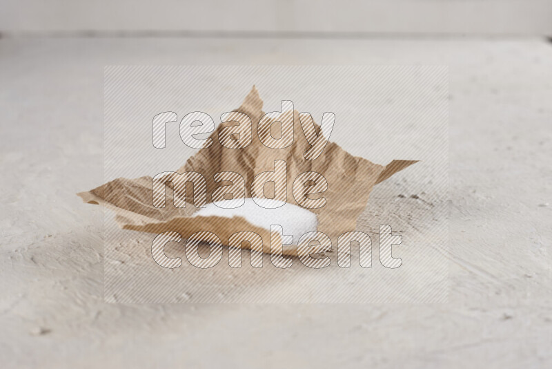 A crumpled piece of paper full of white salt on white background