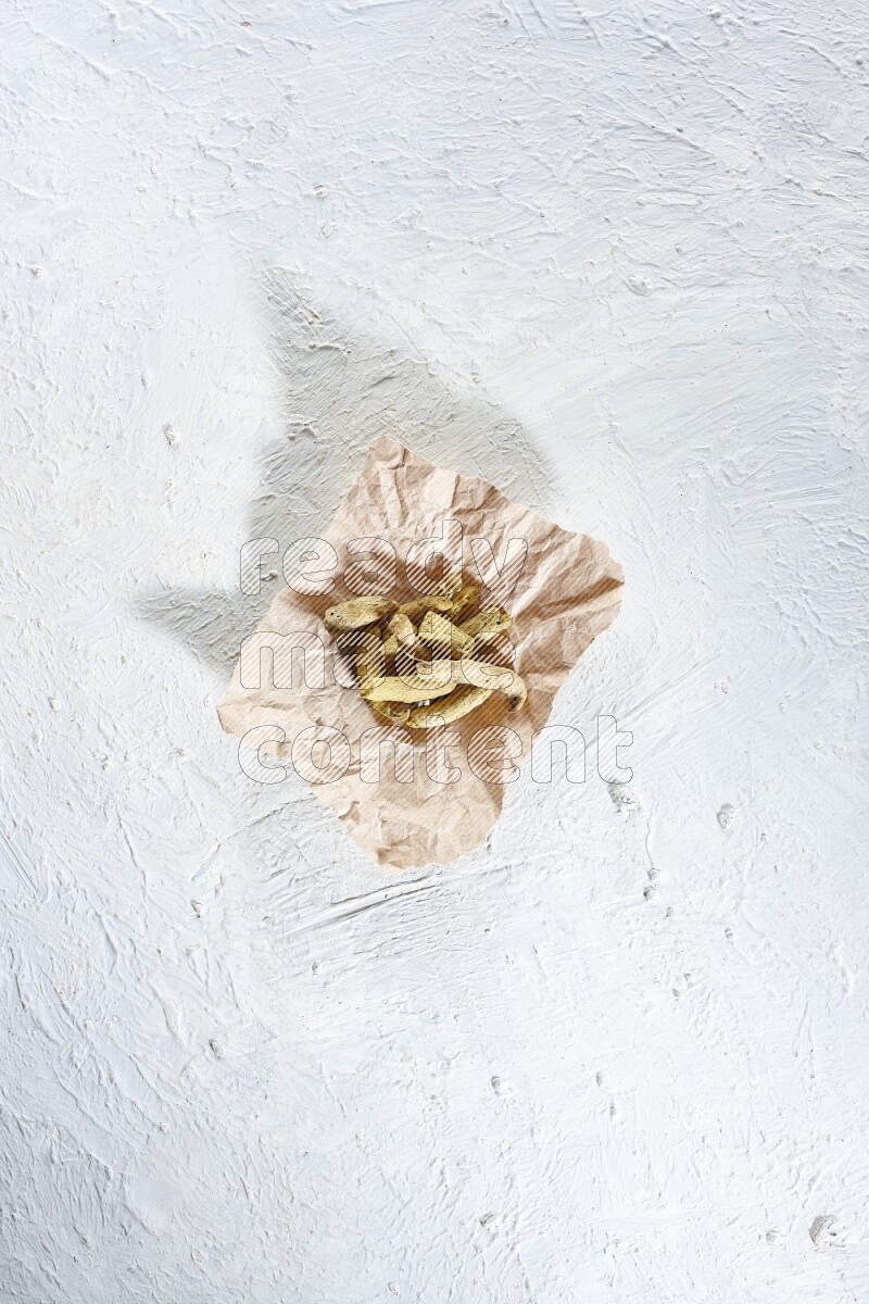 Dried turmeric whole fingers in a crumpled piece of paper on textured white flooring