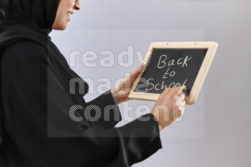 A woman in abaya holding books and a board in different positions (back to school)