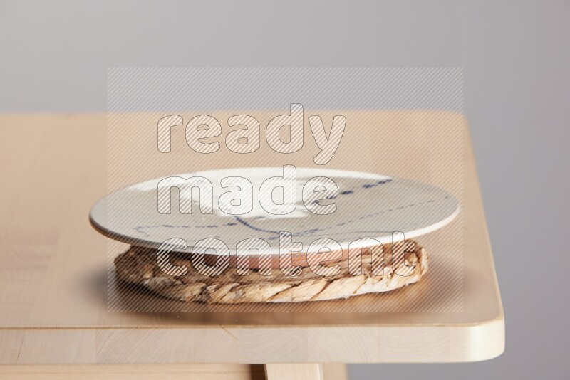multi-colored pottery Plate placed on a small light colored straw placemat on the edge of wooden table