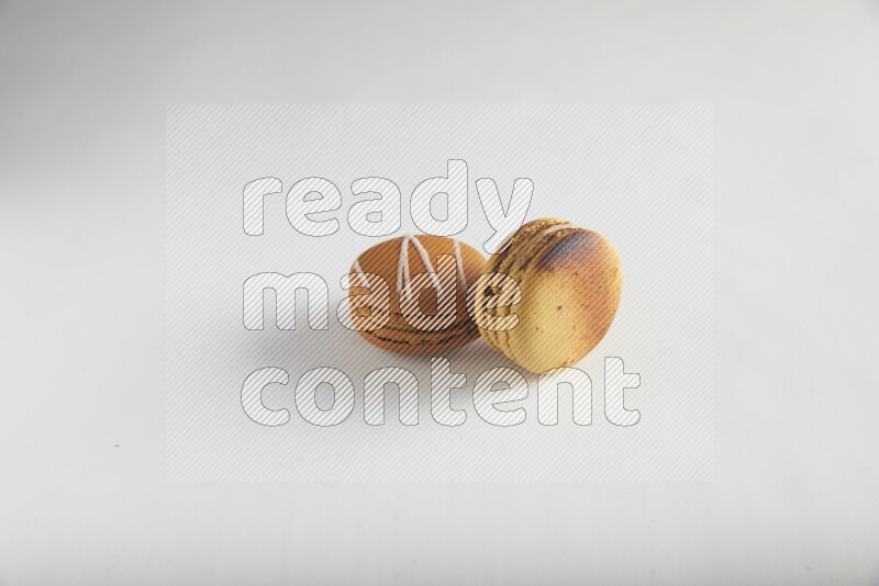 45º Shot of of two assorted Brown Irish Cream, and Yellow Crème Brulée macarons on white background