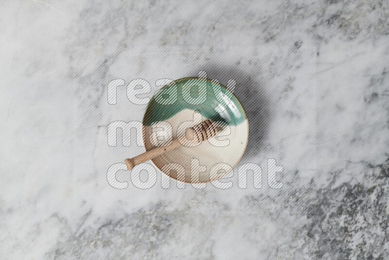 Multicolored pottery plate with wooden honey dipper in it on grey marble background