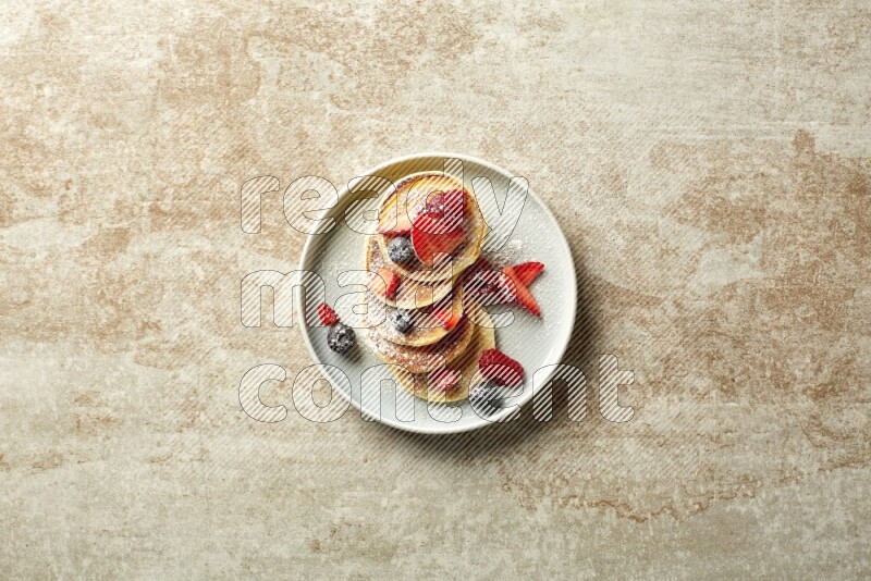 Five stacked mixed berries mini pancakes in a blue plate on beige background
