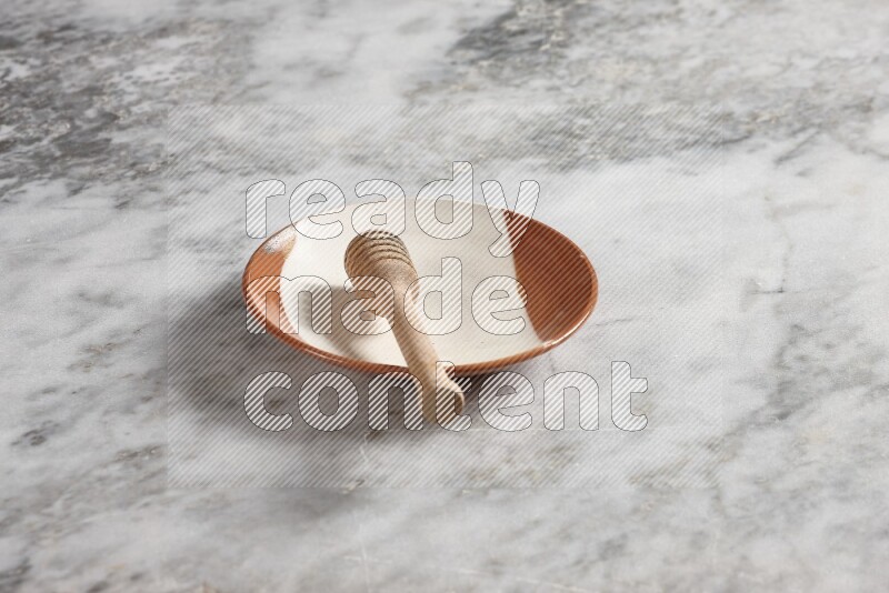Multicolored pottery plate with wooden honey dipper in it on grey marble background