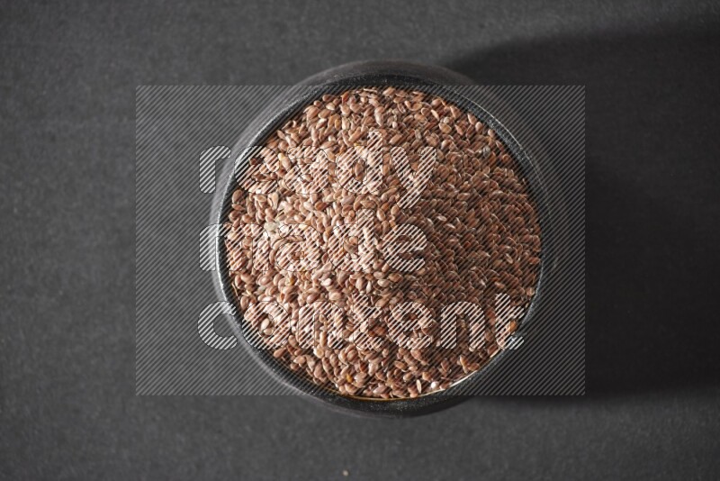 وعاء فخاري أسود ممتلئ بحبوب بذر الكتان على أرضية سوداء