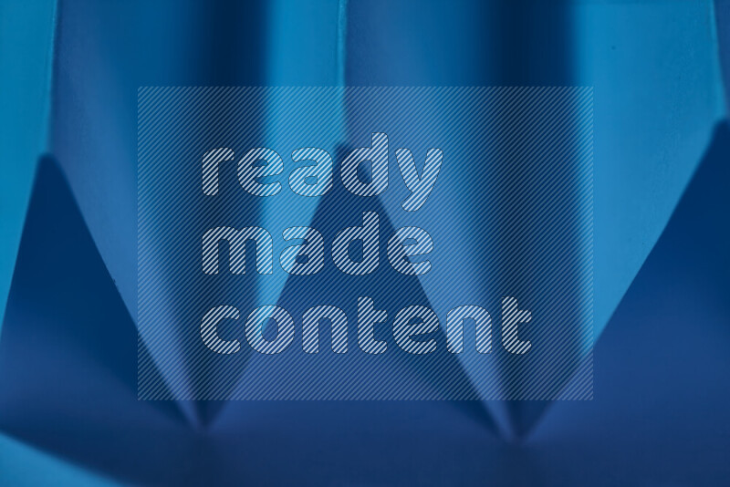 A close-up abstract image showing sharp geometric paper folds in blue gradients