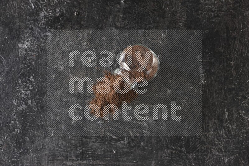 وعاء زجاجي للتوابل مقلوب ممتلئ ببودرة القرنفل والبودرة سقطت منه على أرضية سوداء