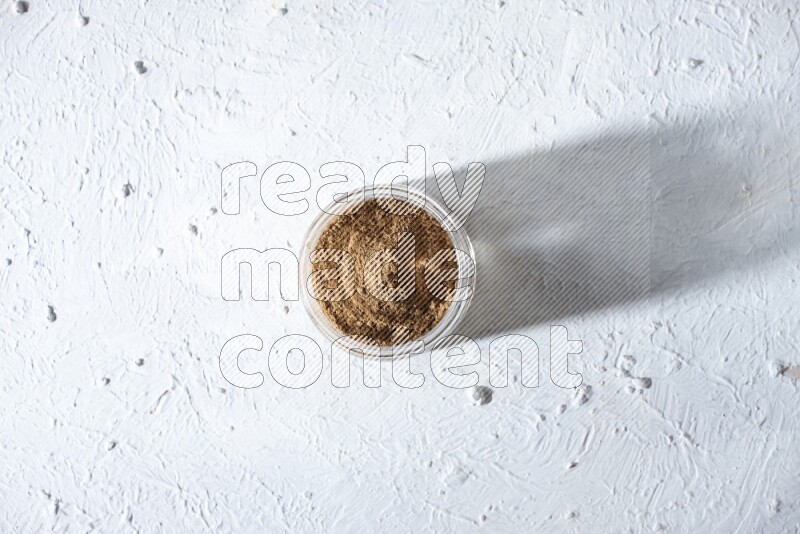 A glass jar full of allspice powder on a textured white flooring
