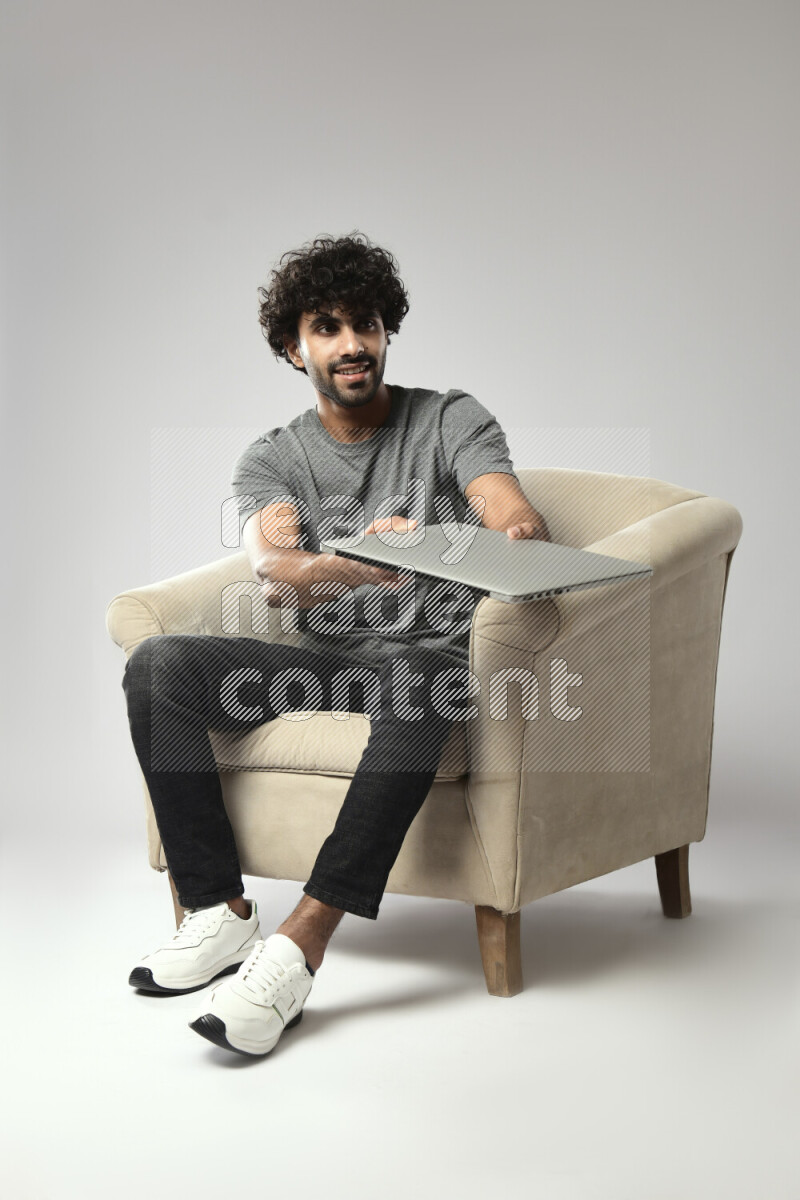 A man wearing casual sitting on a chair holding a laptop on white background