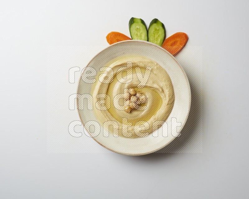 Hummus in a pottry plate garnished with roasted chickpeas on a white background
