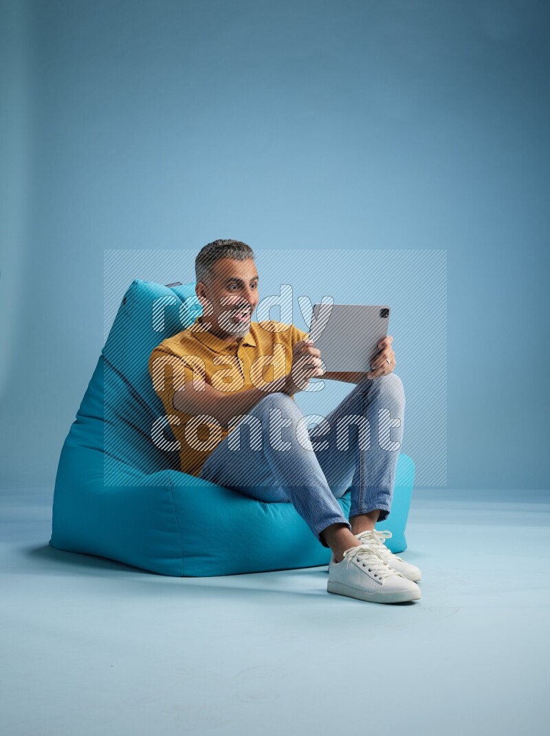 A man sitting on a blue beanbag and working on tablet