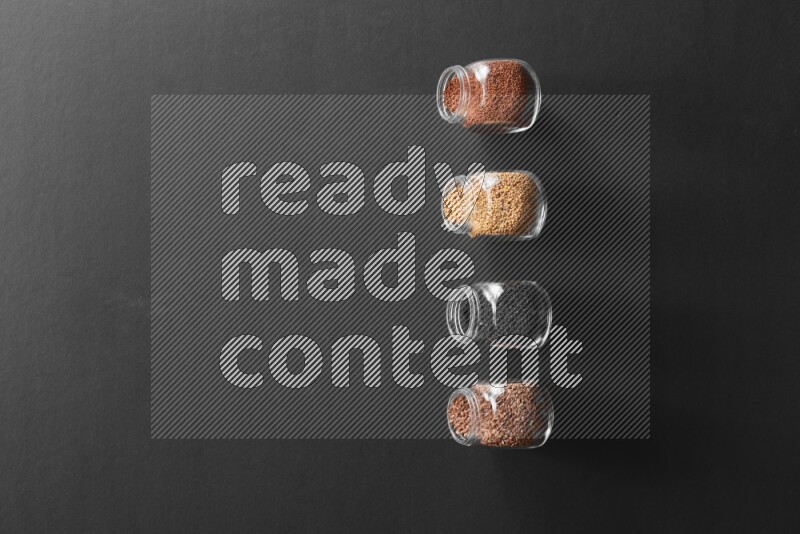 4 glass spice jars full of black seeds, mustard seeds, flax and garden cress on black flooring