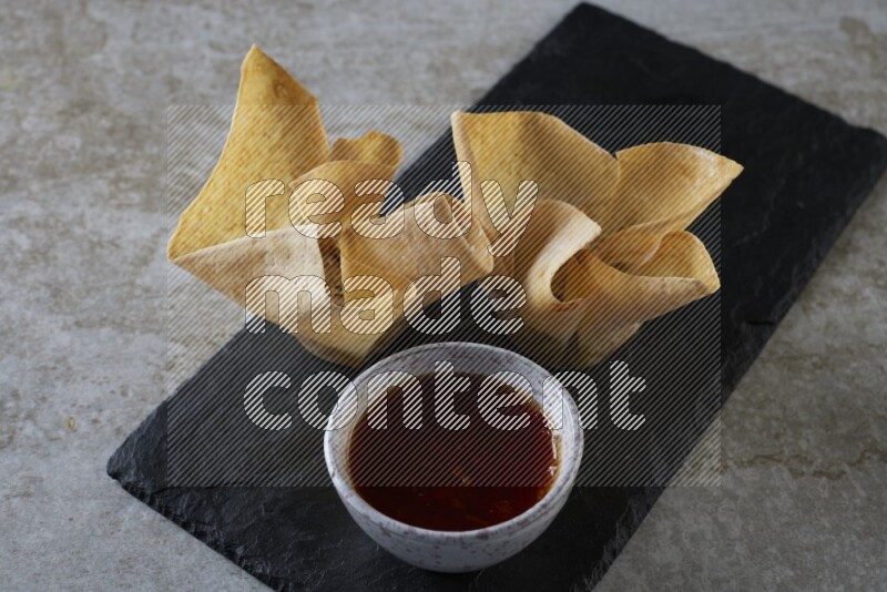 wonton cups with soy sauce ramkin on rectangle slate on grey textured counter top