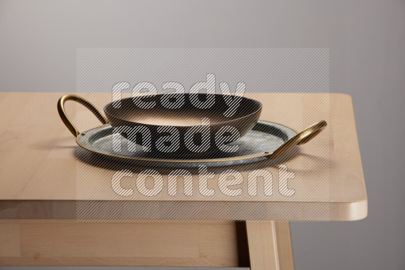 brass plate placed on a rounded stainless steel tray with golden handels on the edge of wooden table