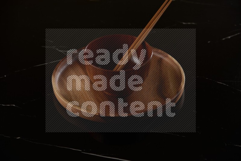 brown wood round bowl on top of brown wood round plate on black marble countertop